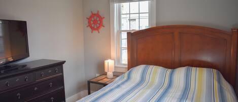 Un dormitorio con cama, cómoda, televisor, ventana y un adorno en la pared.
