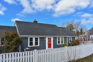 Ein Haus mit roter Tür, weißem Zaun und blauem Himmel.
