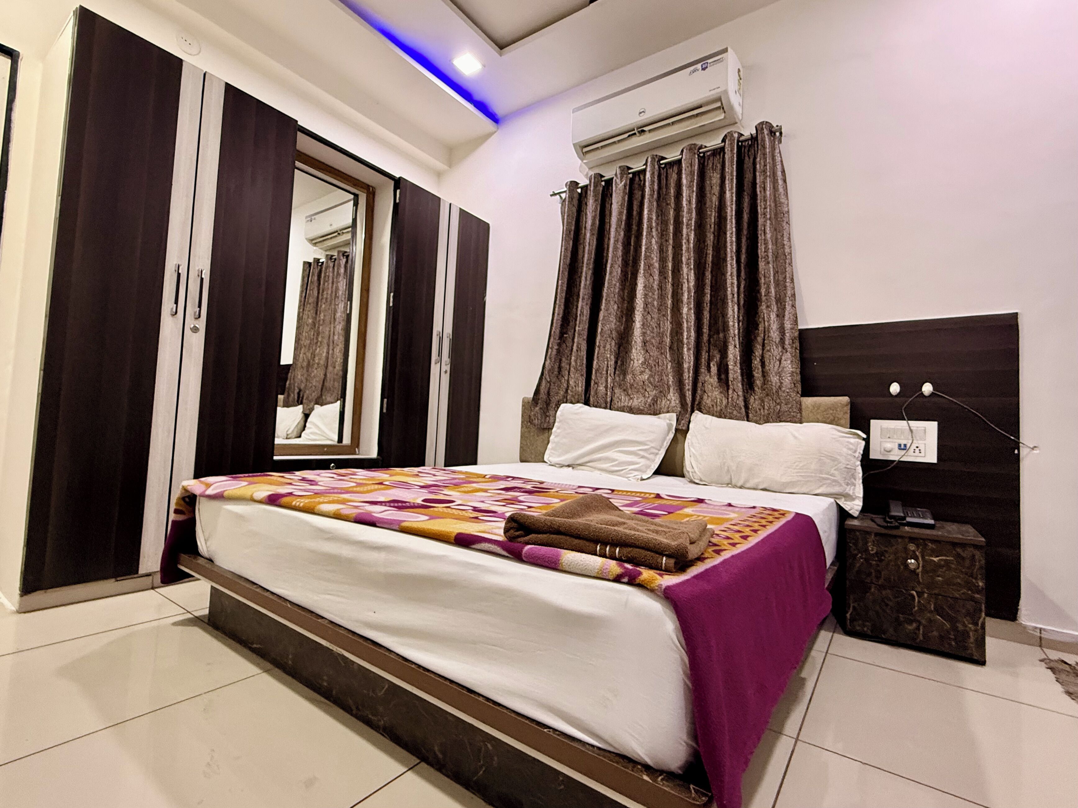 A bedroom with a bed, a wardrobe, an air conditioning unit, a nightstand, and a mirror.