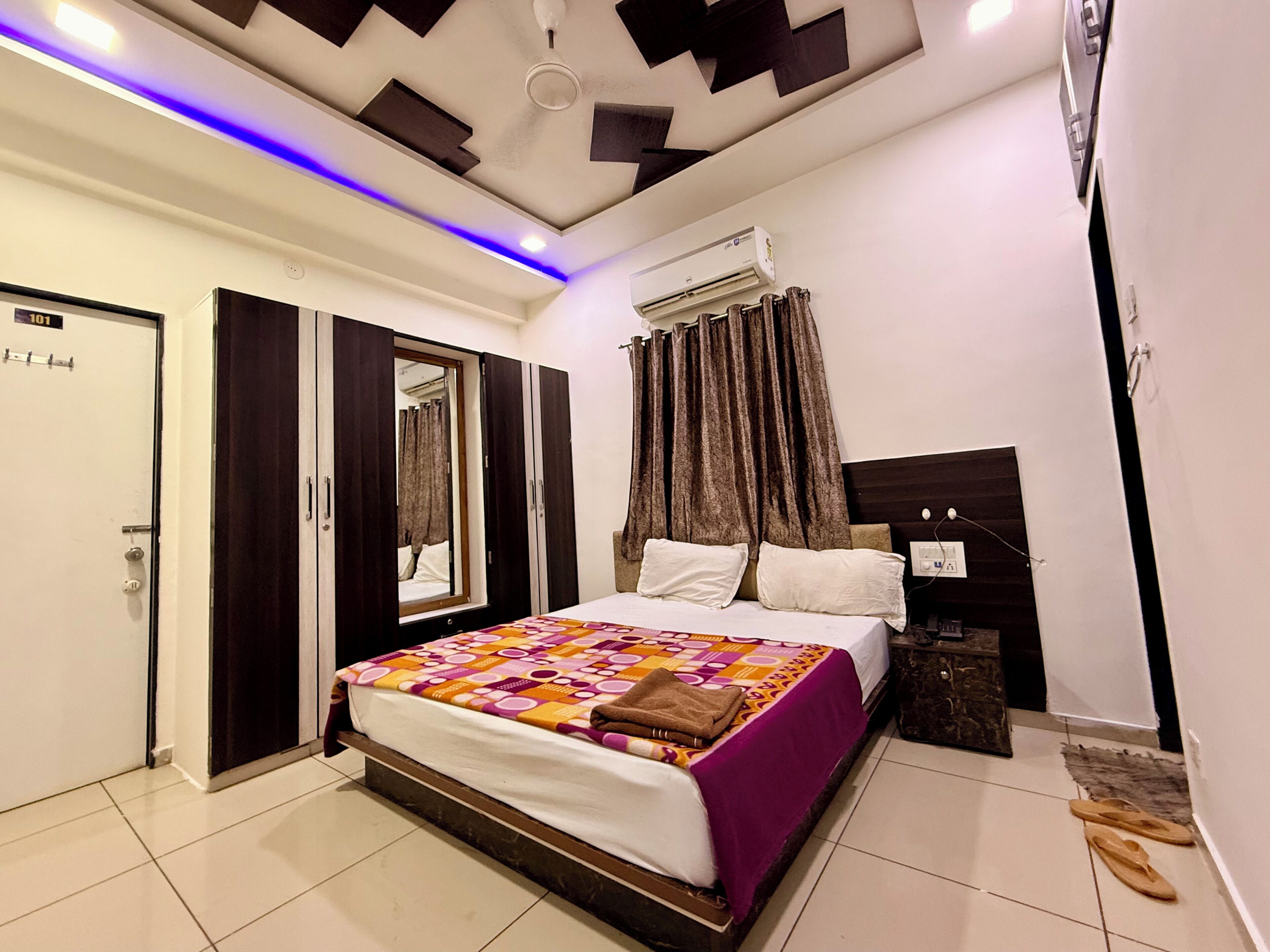 A bedroom with a bed, a wardrobe, a mirror, a ceiling fan, and an air conditioning unit.