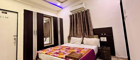 A bedroom with a bed, a wardrobe, a mirror, a ceiling fan, and an air conditioning unit.