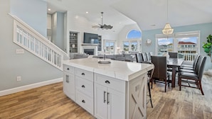 Un'ampia cucina con una grande isola, una zona pranzo con un tavolo e sedie in legno scuro, e una scala che conduce a un altro piano.
