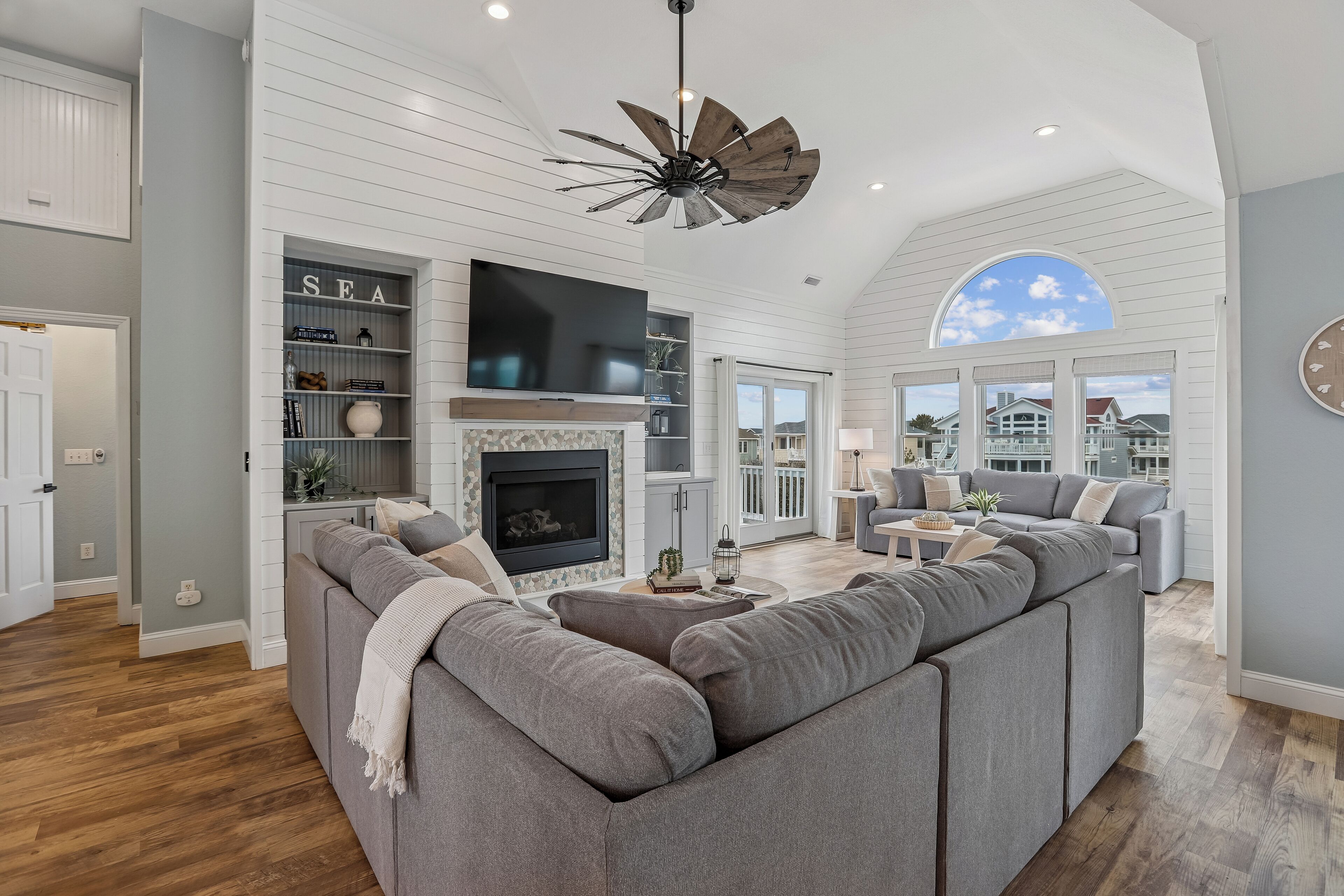 A spacious living room with a large sectional sofa, a fireplace, a mounted TV, and a ceiling fan.