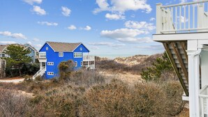 Una casa blu con un balcone, circondata da vegetazione secca e un cielo sereno.