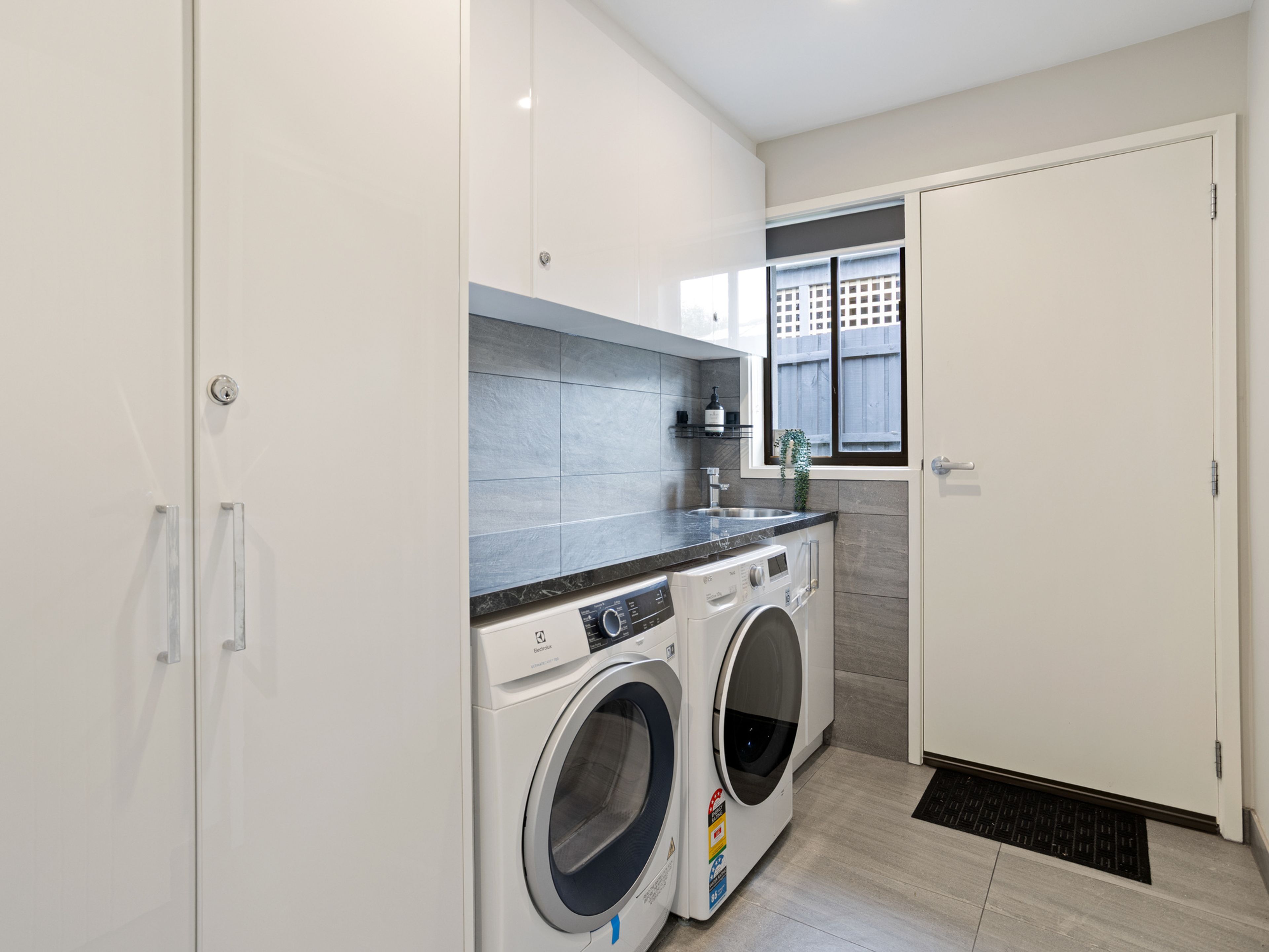 A modern laundry room with a washing machine, dryer, and a small window.