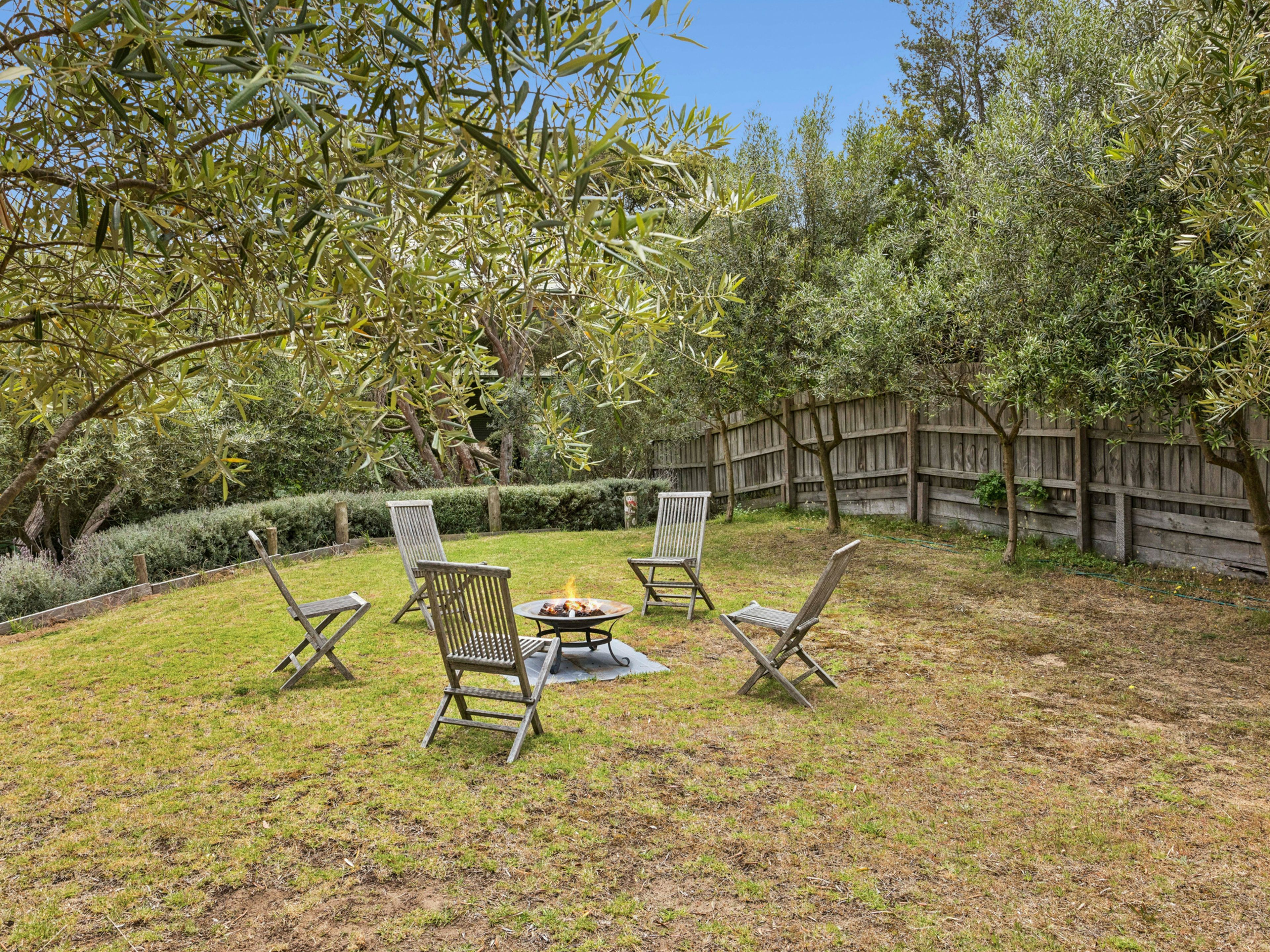 A backyard with a fire pit, three chairs, and a wooden fence.