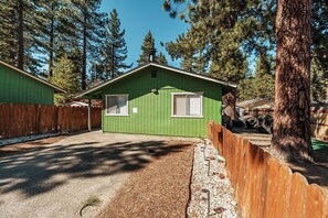 Eine grüne Holzhütte mit zwei Fenstern, umgeben von einem Holzzaun und hohen Bäumen.