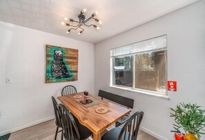 Ein Essbereich mit Holztisch, schwarzen Stühlen, einem Bild an der Wand, einem Fenster mit Jalousien und einer Deckenleuchte.