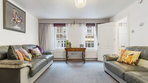 Ein Wohnzimmer mit zwei Ledersofas, einem Holztisch und einem großen Fenster mit Vorhängen.