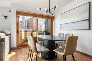A dining area with a round table and six chairs, a wooden floor, and a large window with blinds. - Ski-in / Walk to Lift, Trails & Main St / Hot Tubs & Pool / Kid-Friendly (Breckenridge)