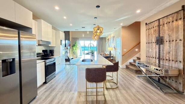 A modern kitchen with stainless steel appliances, a central island with bar stools, and a wooden accent wall. - Brand New Home with 4 En-Suites, near Disney (Kissimmee)