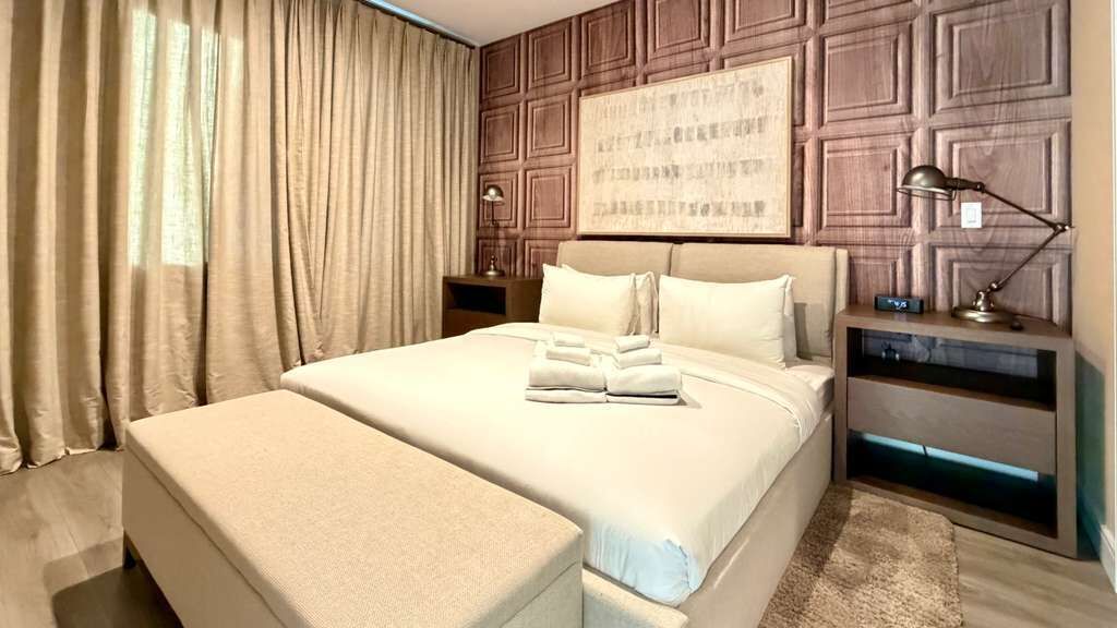 Een hotelkamer met een groot bed, een nachtkastje met een lamp, een wandlamp en een kunstwerk aan de muur.