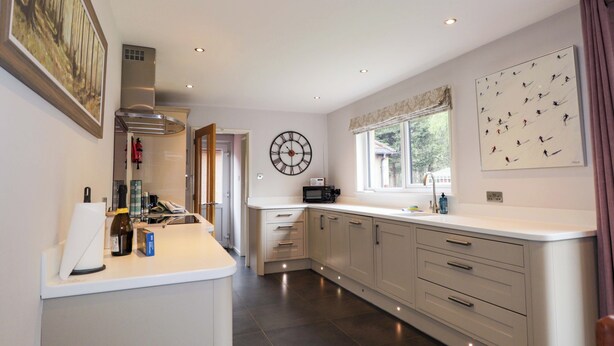 A modern kitchen with a central island, a large clock, and a window with a view. - 6 Carn Dearg (Aviemore)