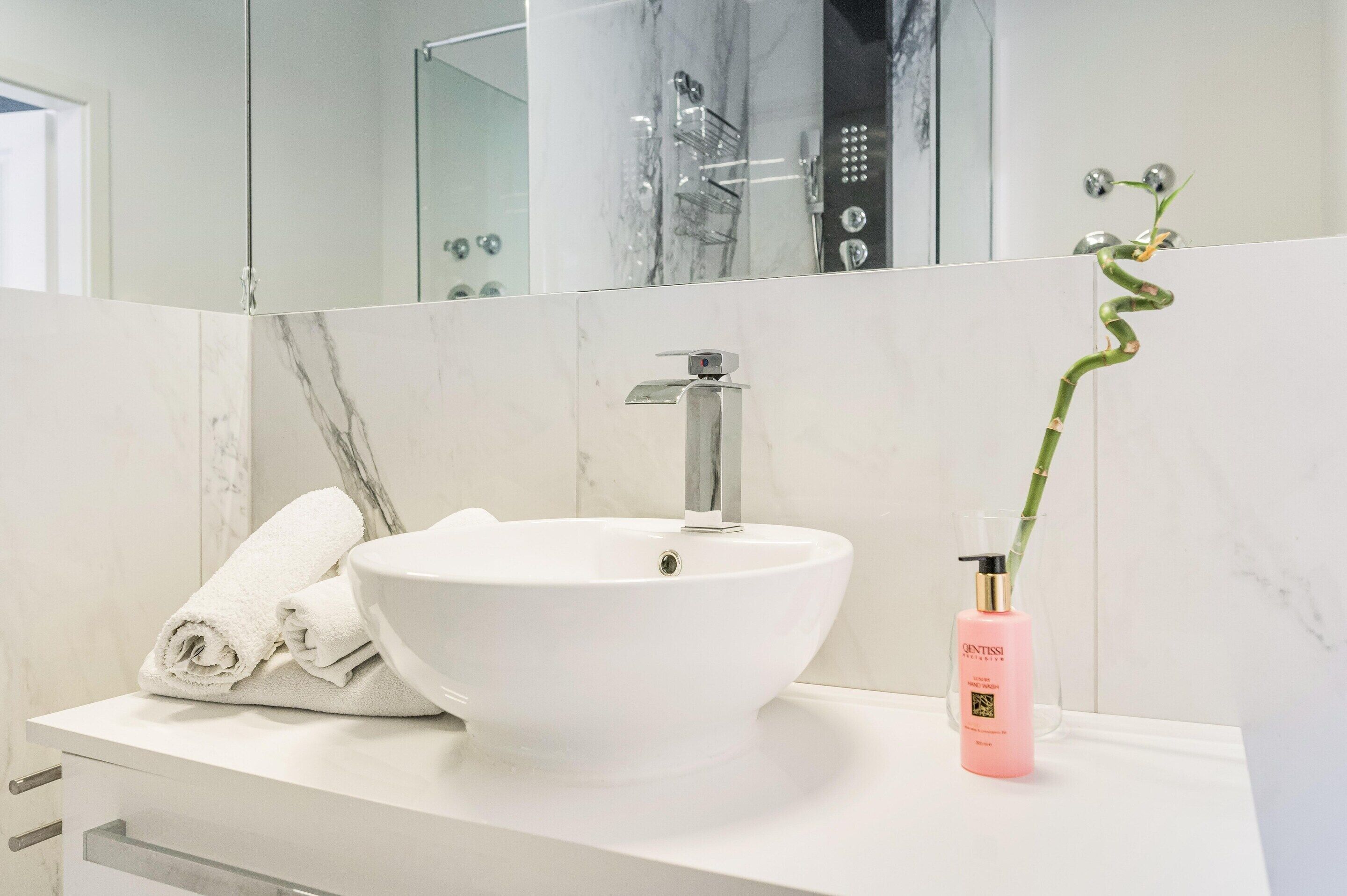 Een badkamer met een wit wastafel, een spiegel, een douche en een flesje lotion.