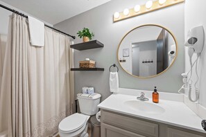 A bathroom with a toilet, sink, and mirror. There are shelves above the toilet with a plant and a basket. - Private Parking, Fire Ring, King Beds - Near Ark! (Dry Ridge)