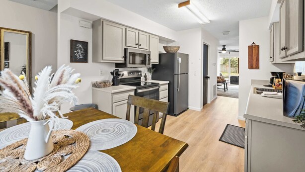 A modern kitchen with white cabinets, a black refrigerator, and a microwave. There is a dining table with a vase of pampas grass. - Private Parking, Fire Ring, King Beds - Near Ark! (Dry Ridge)
