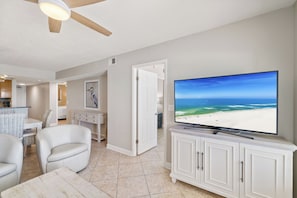 A living room with a large flat-screen TV, white furniture, and a view of the ocean. - Boardwalk 585 by Liquid Life (Gulf Shores)