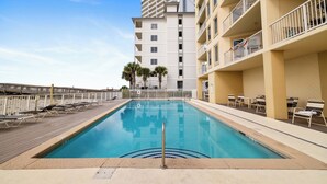 A swimming pool with lounge chairs and a wooden deck, surrounded by a multi-story building with balconies. - Boardwalk 886 by Liquid Life (Gulf Shores)