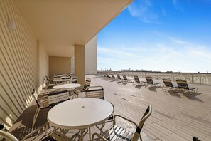 A sunlit outdoor seating area with tables and chairs, overlooking a waterfront. - Boardwalk 886 by Liquid Life (Gulf Shores)