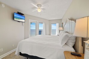 Une chambre d’hôtel avec un lit, un ventilateur de plafond, un téléviseur fixé au mur et une fenêtre donnant sur la plage.