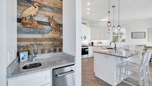 A modern kitchen with a wooden accent wall, stainless steel appliances, and a central island with bar stools. - Beachfront | Pet Friendly | Shared Pool, Elevator (Fort Morgan)