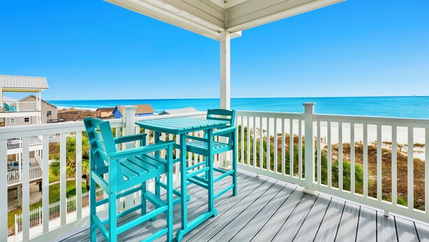 A wooden deck with a table and chairs, overlooking a beach with a clear blue sky. - Beachfront | Pet Friendly | Shared Pool, Elevator (Fort Morgan)