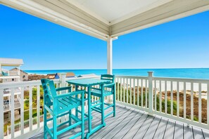 A wooden deck with a table and chairs, overlooking a beach with a clear blue sky. - Beachfront | Pet Friendly | Shared Pool, Elevator (Fort Morgan)