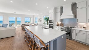 Una cocina espaciosa con una isla grande, armarios blancos y vista al océano.