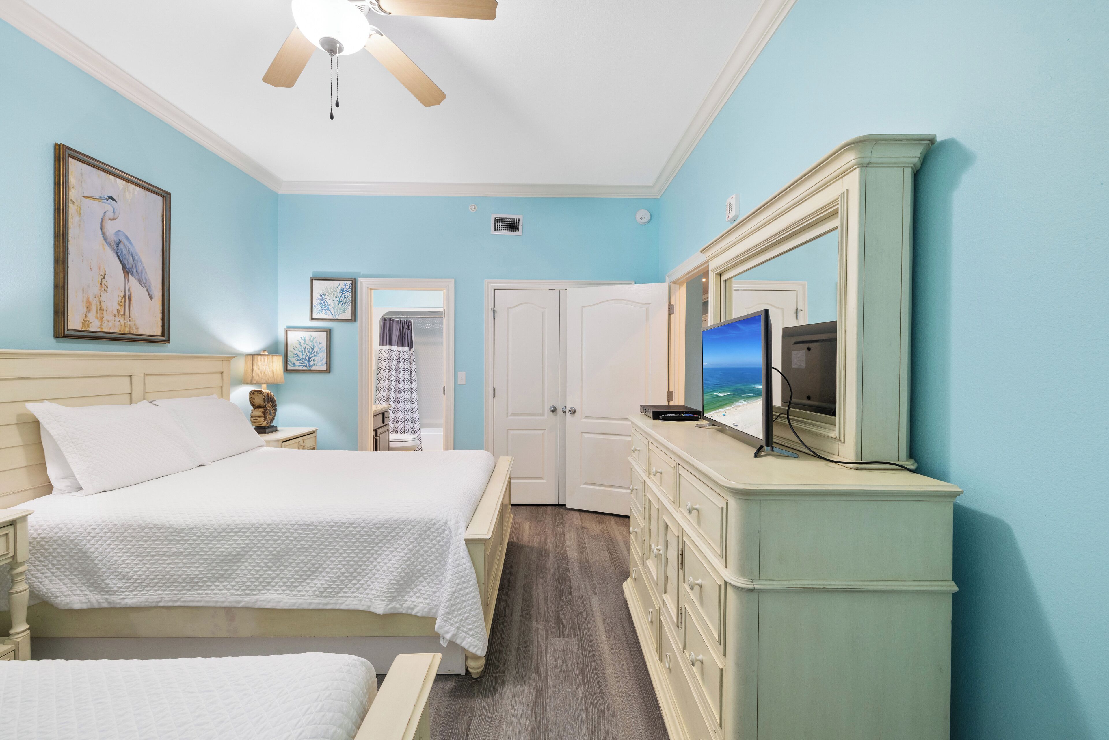A bedroom with a bed, dresser, TV, and artwork.