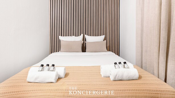 Ein Hotelzimmer mit einem Bett, zwei Kissen, einem gestreiften Kopfteil und Handtüchern mit Flaschen auf dem Bett.