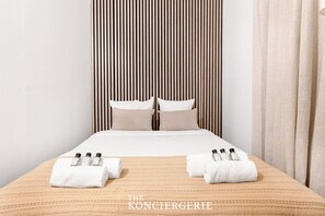 A hotel room with a bed, two pillows, a striped headboard, and towels with bottles on the bed. - Charmant studio au cœur du Marais (Paris)