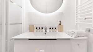 Ein modernes Badezimmer mit einem weißen Waschtisch, einem runden Spiegel und mehreren Parfumflaschen.
