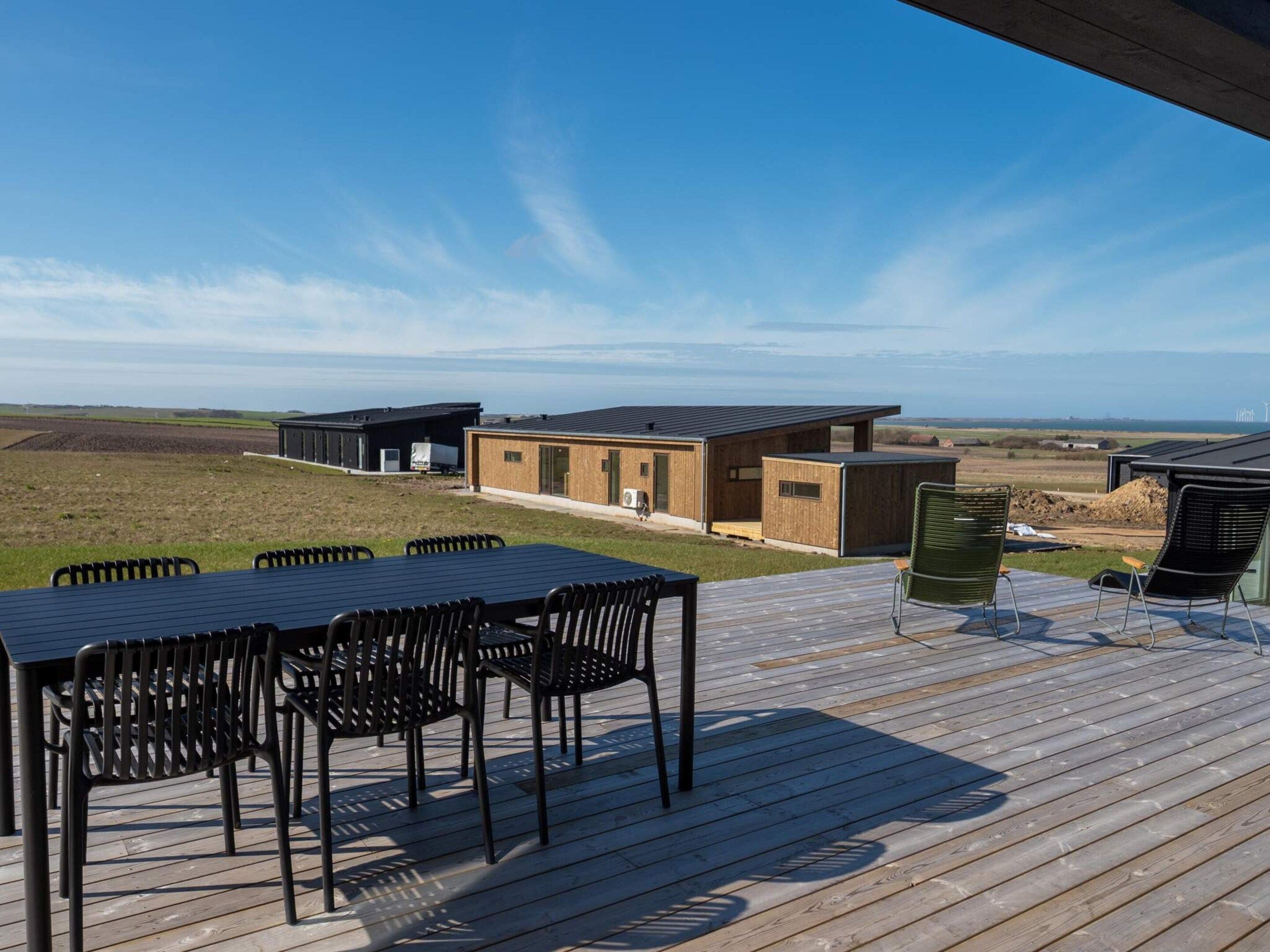 Een terras met een tafel en stoelen, met uitzicht op een kustlandschap met gebouwen.