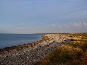 A coastal landscape with a pebble beach leading to the sea, surrounded by grassy fields. - 5 Star Holiday Home in Lemvig (Lemvig)