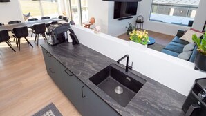 A modern kitchen with a large island, a dining area with chairs, a sofa, and a TV mounted on the wall. - 5 Star Holiday Home in Lemvig (Lemvig)