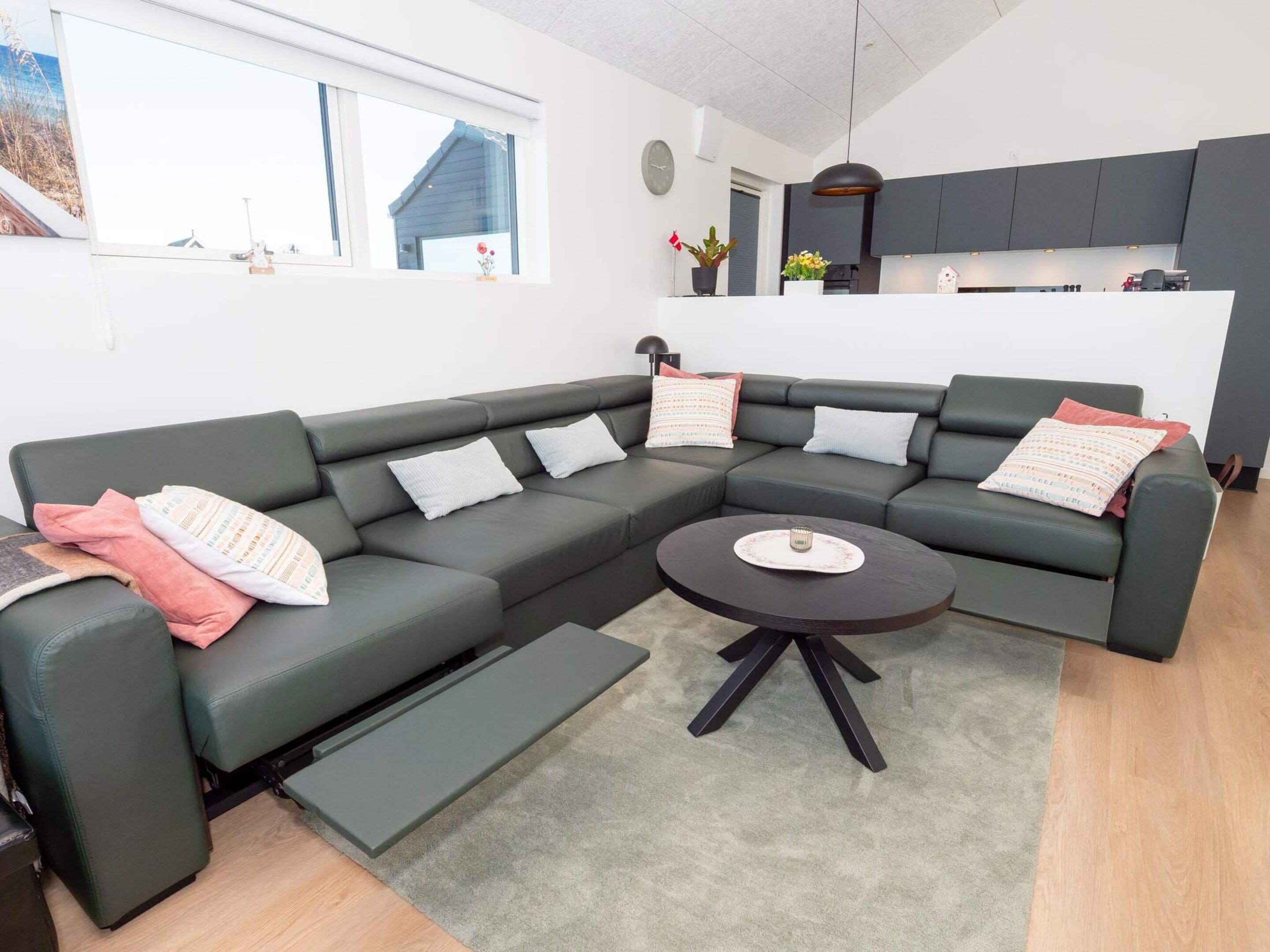 A modern living room with a sectional sofa, a coffee table, and a kitchen in the background.