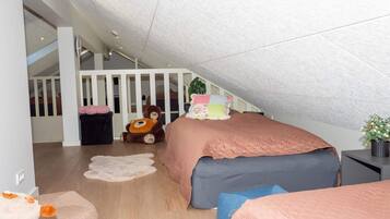 A child's bedroom with a sloped ceiling, a bed with a pink and blue bedspread, a teddy bear, and a small potted plant.