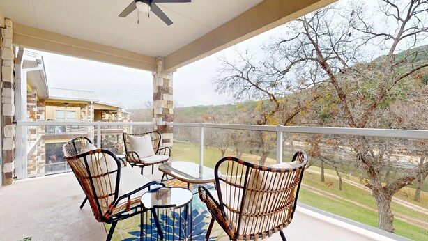 A covered outdoor area with wicker chairs and a table, overlooking a residential area and trees. - River City Resorts: Rio Guad 313: Remarkable Condo, Guadalupe River View! (New Braunfels)