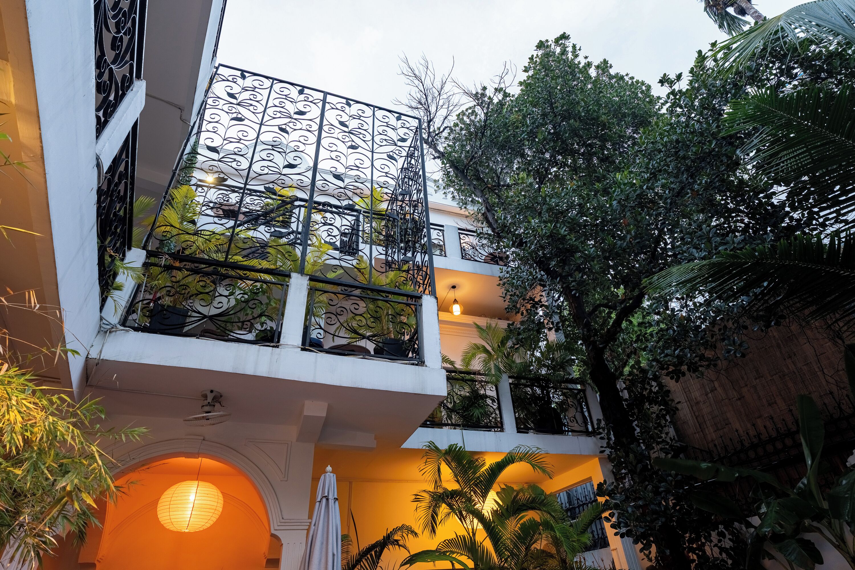 A multi-level building with balconies, outdoor lighting, and lush greenery.
