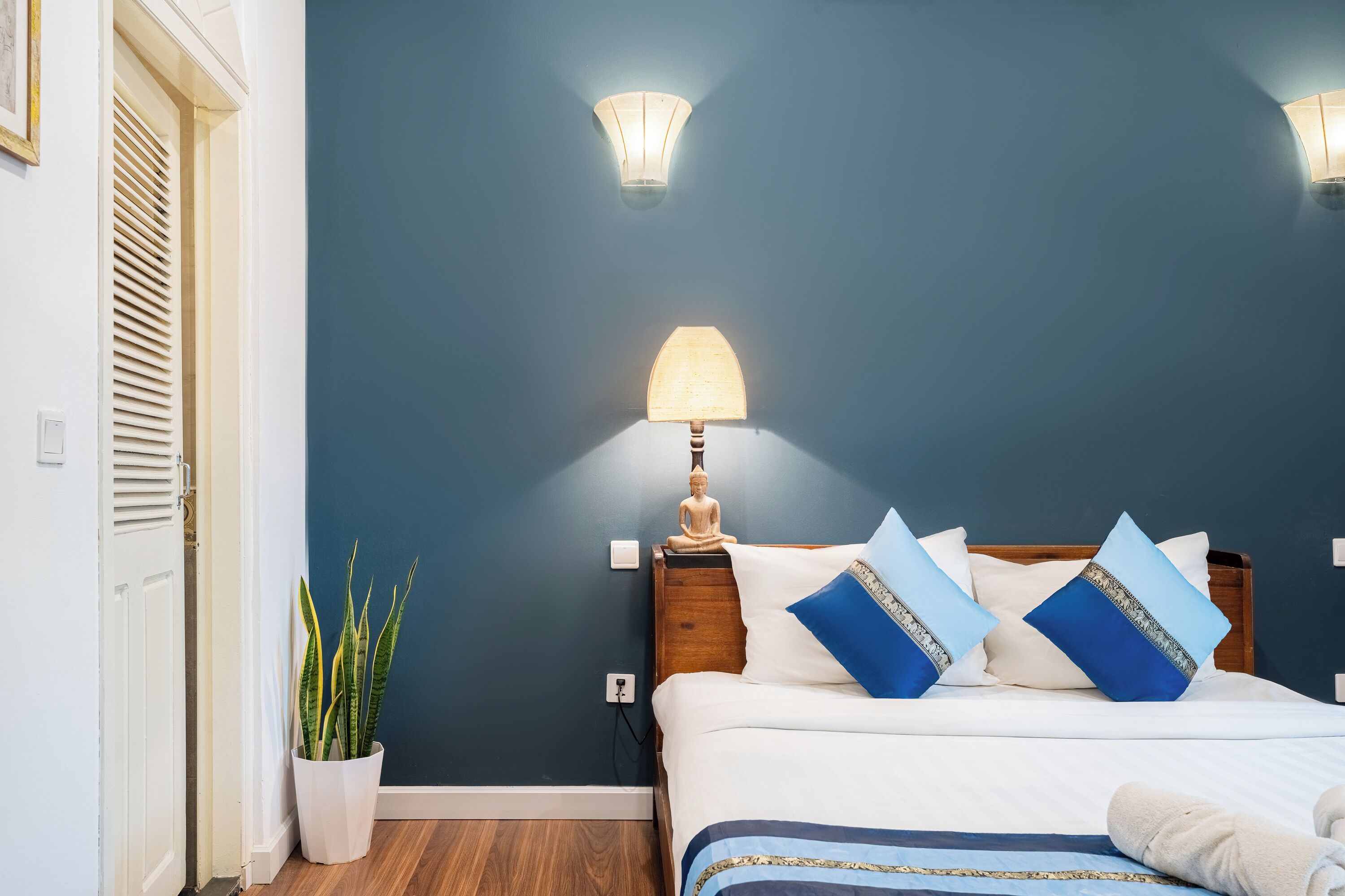 A bedroom with a bed, bedside lamp, and a potted plant.