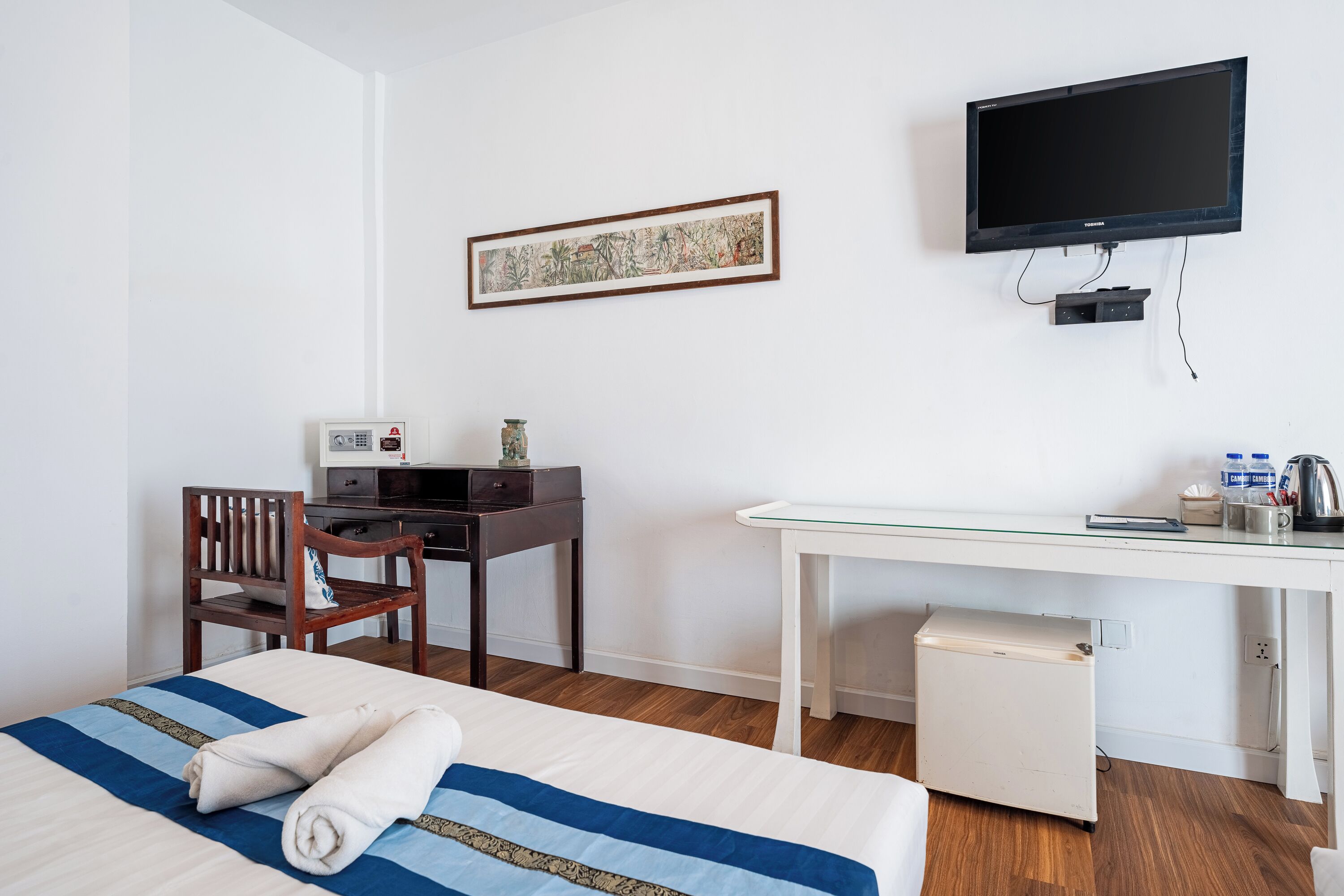 A hotel room with a bed, a desk, a chair, a television, and a small refrigerator.
