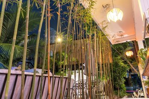 Una estructura de bambú con luces colgantes, una silla blanca y una mesa en un entorno al aire libre.