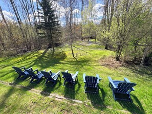 A grassy area with several Adirondack chairs arranged in a row. - Private Creekside Retreat on 5 Acres 4BR-3BA Minutes to Boyne Mountain (East Jordan)