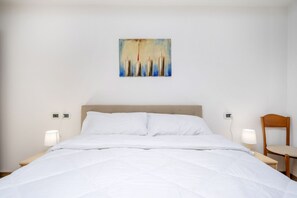 A hotel room with a bed, two bedside tables with lamps, a wooden chair, and a painting on the wall. - GuestHost - Comfortable 69 sqm apartment, perfect for groups or families of up to 4 guests, located on the ground floor of a historic building (a few steps to access).The apartment is located just outside the centre of Udine, a perfect alternative for th (Udine)