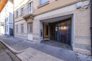 A building with a gated entrance, a small balcony, and a paved sidewalk.