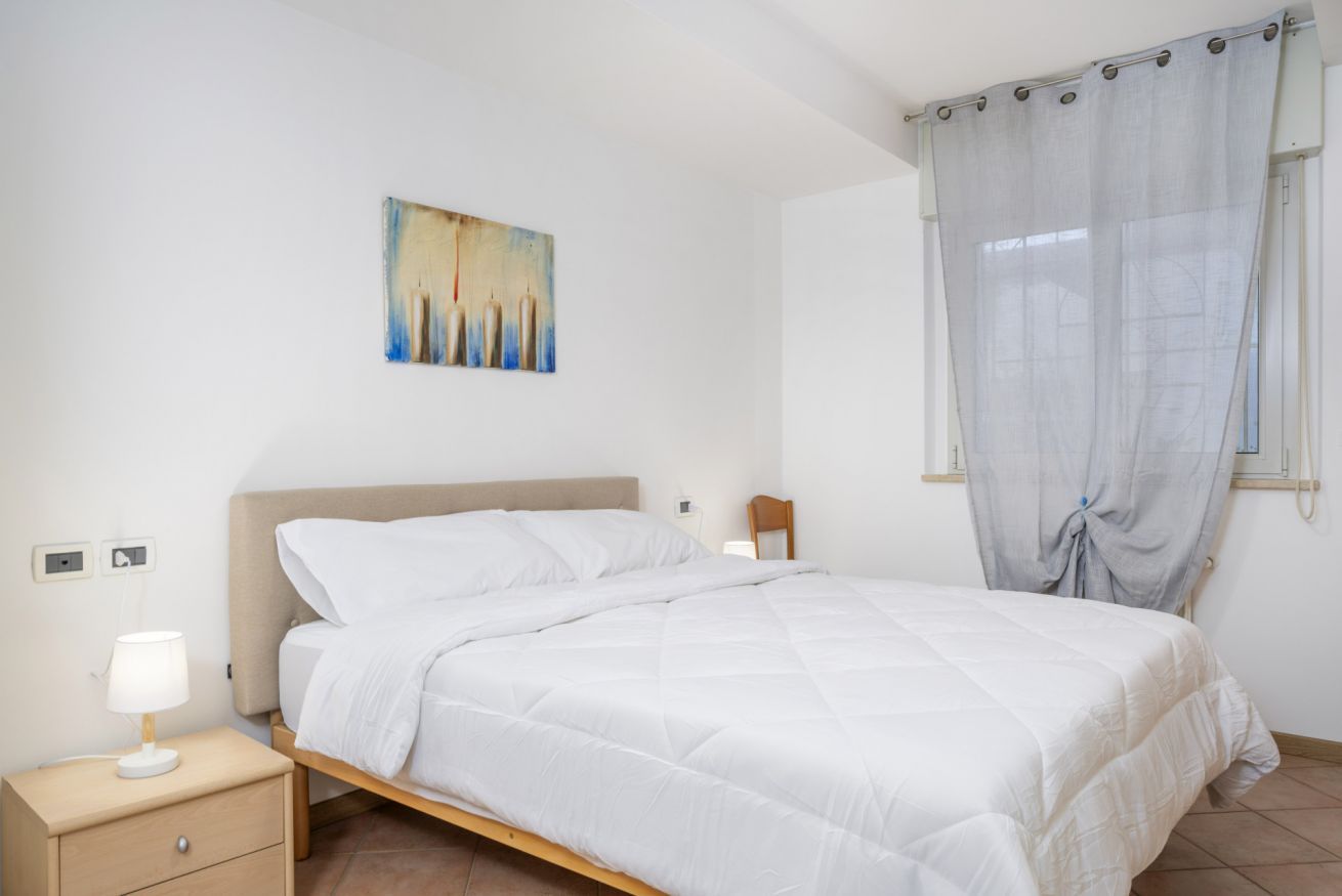 A bedroom with a bed, bedside table, lamp, and a painting on the wall.
