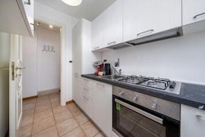 Una cocina con gabinetes blancos, estufa a gas, horno y piso de baldosas.
