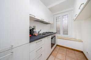 A compact kitchen with white cabinets, a black countertop, a gas stove, and a window with frosted glass. - GuestHost - Comfortable 69 sqm apartment, perfect for groups or families of up to 4 guests, located on the ground floor of a historic building (a few steps to access).The apartment is located just outside the centre of Udine, a perfect alternative for th (Udine)
