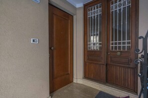 A wooden door with a metal gate, a light switch, and a doormat. - GuestHost - Comfortable 69 sqm apartment, perfect for groups or families of up to 4 guests, located on the ground floor of a historic building (a few steps to access).The apartment is located just outside the centre of Udine, a perfect alternative for th (Udine)