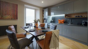 A modern kitchen with a dining area, featuring a large window, a radiator, and a kitchen island with a sink and countertop.